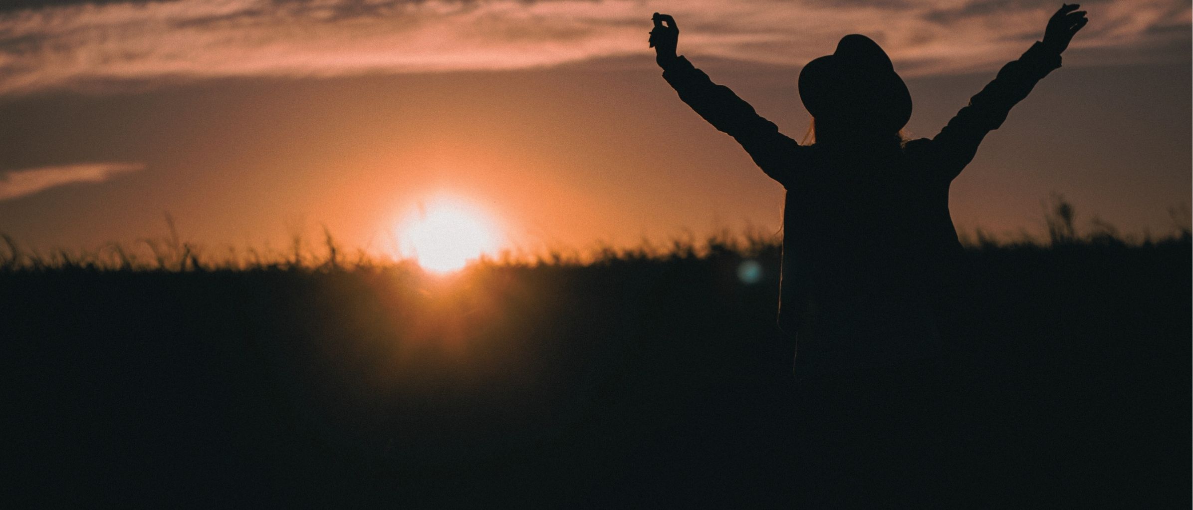 Frau im Sonnenuntergang breitet die Arme aus